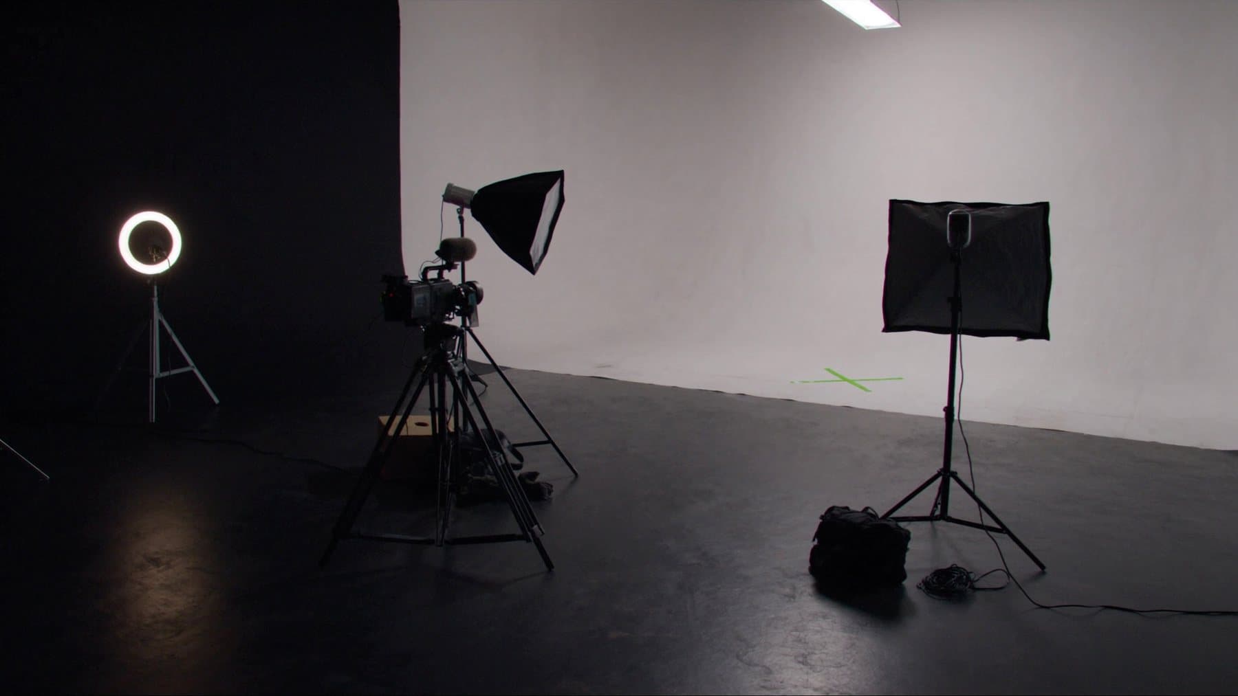 The Kliqx studio set: a white cyc wall, softboxes, a ring light and a camera on a tripod, with a lime tape X on the floor